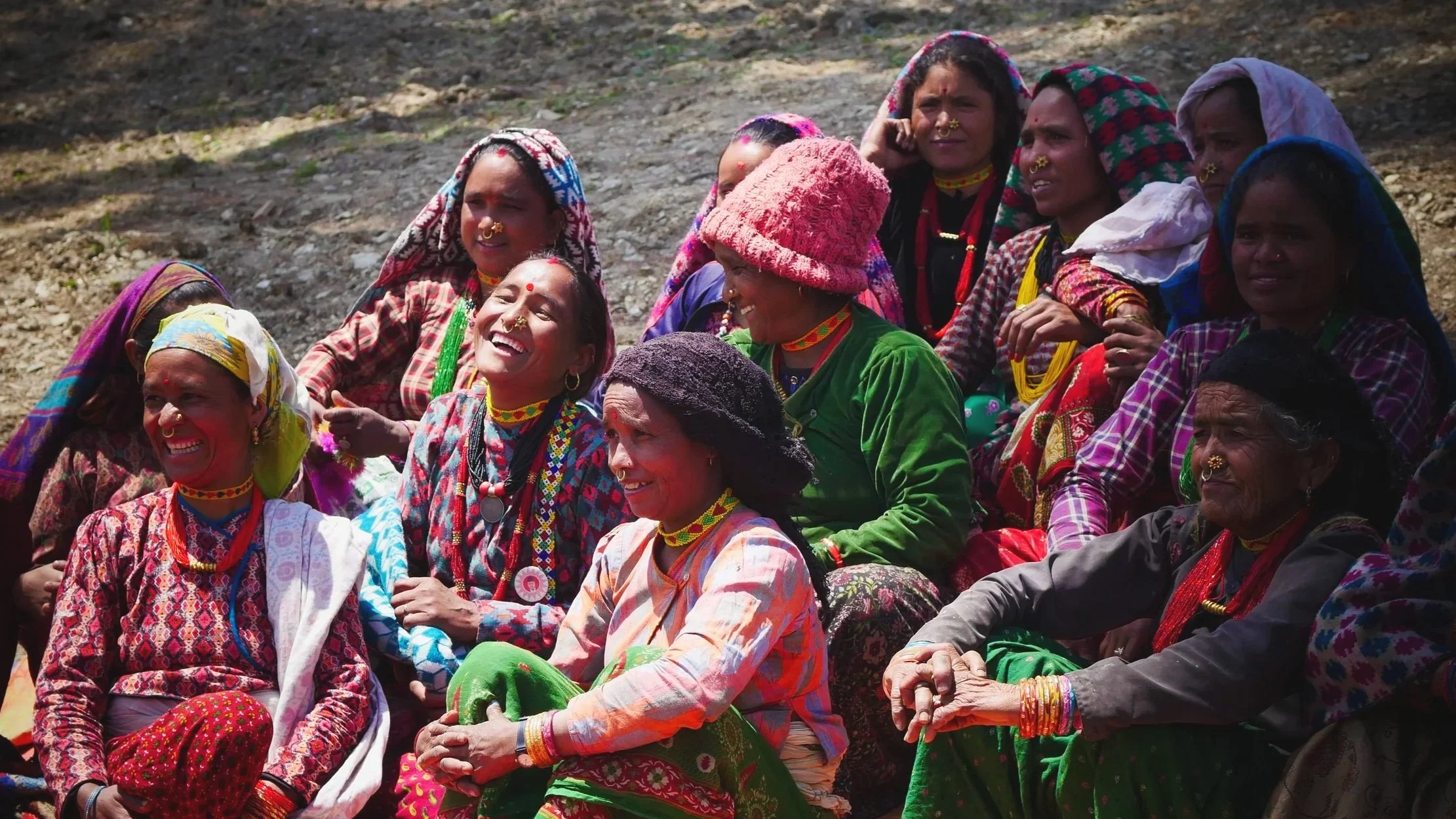 A group of women in colorful traditional dress sitting together and smiling outdoors in Mugu, Nepal