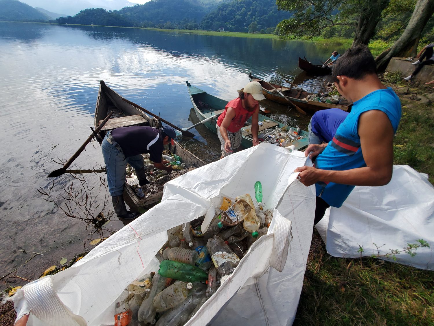 Community members gather along a lakeshore to sort and remove waste from the water